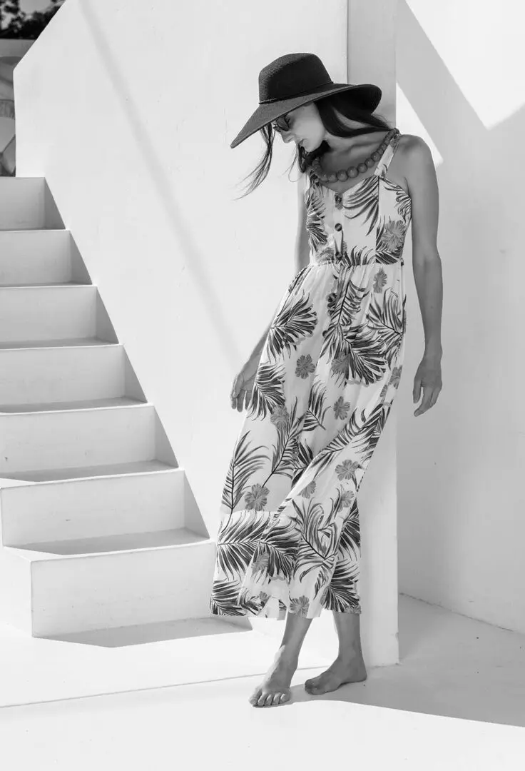 Woman in floral dress and hat standing.